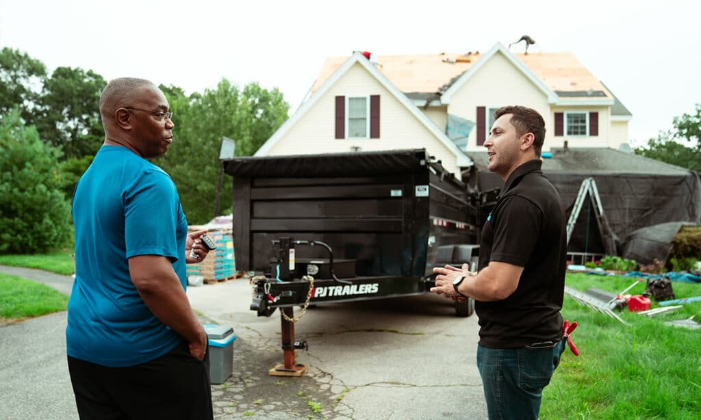 Homeowner consulting a shingle roof repair company, reviewing licenses, warranties, and client references for quality assurance.