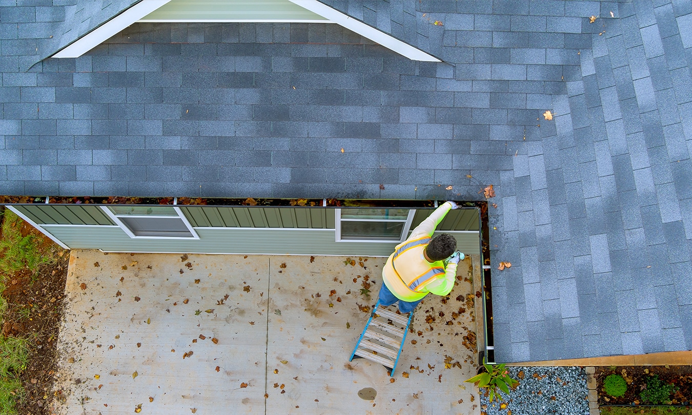 Roofer clearing gutters as part of seasonal maintenance to prevent roof damage.